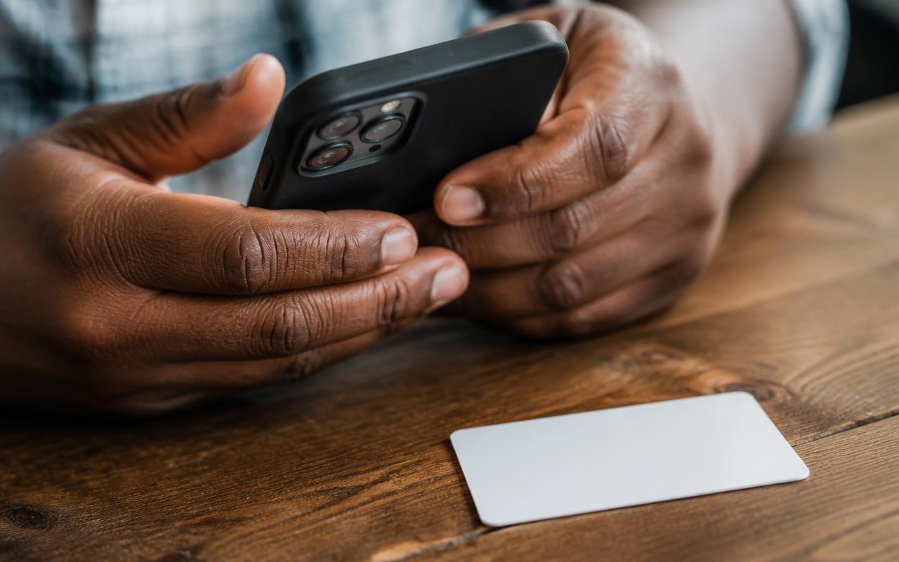 Hands holding a phone beside an identity card on a wooden table